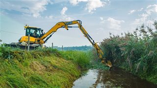 Gras uit beek halen met machine