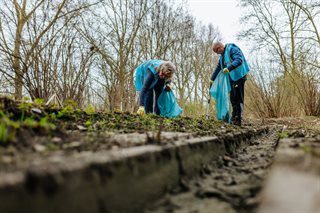 Twee personen ruimen afval langs waterkant op